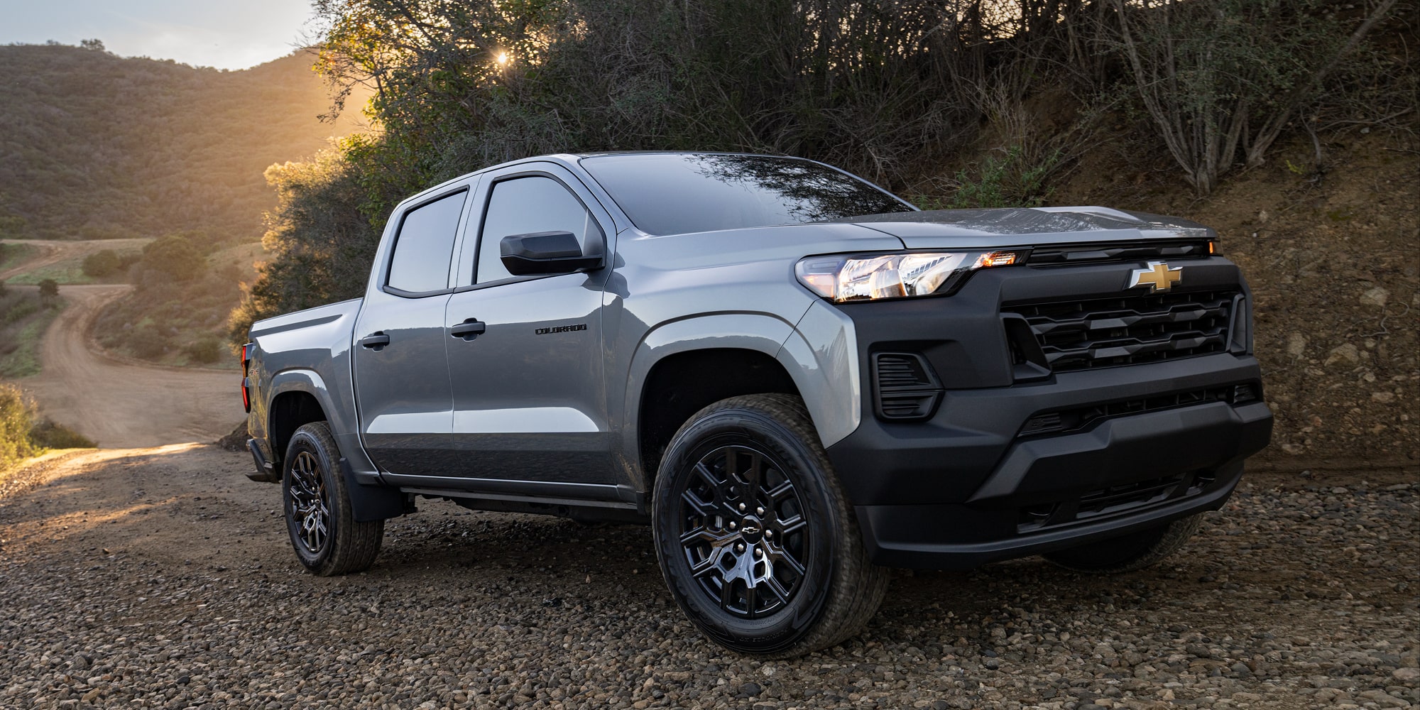 A Chevy Colorado Parked on a Rocky Dirt Road With Trees and Mountains in the Background.