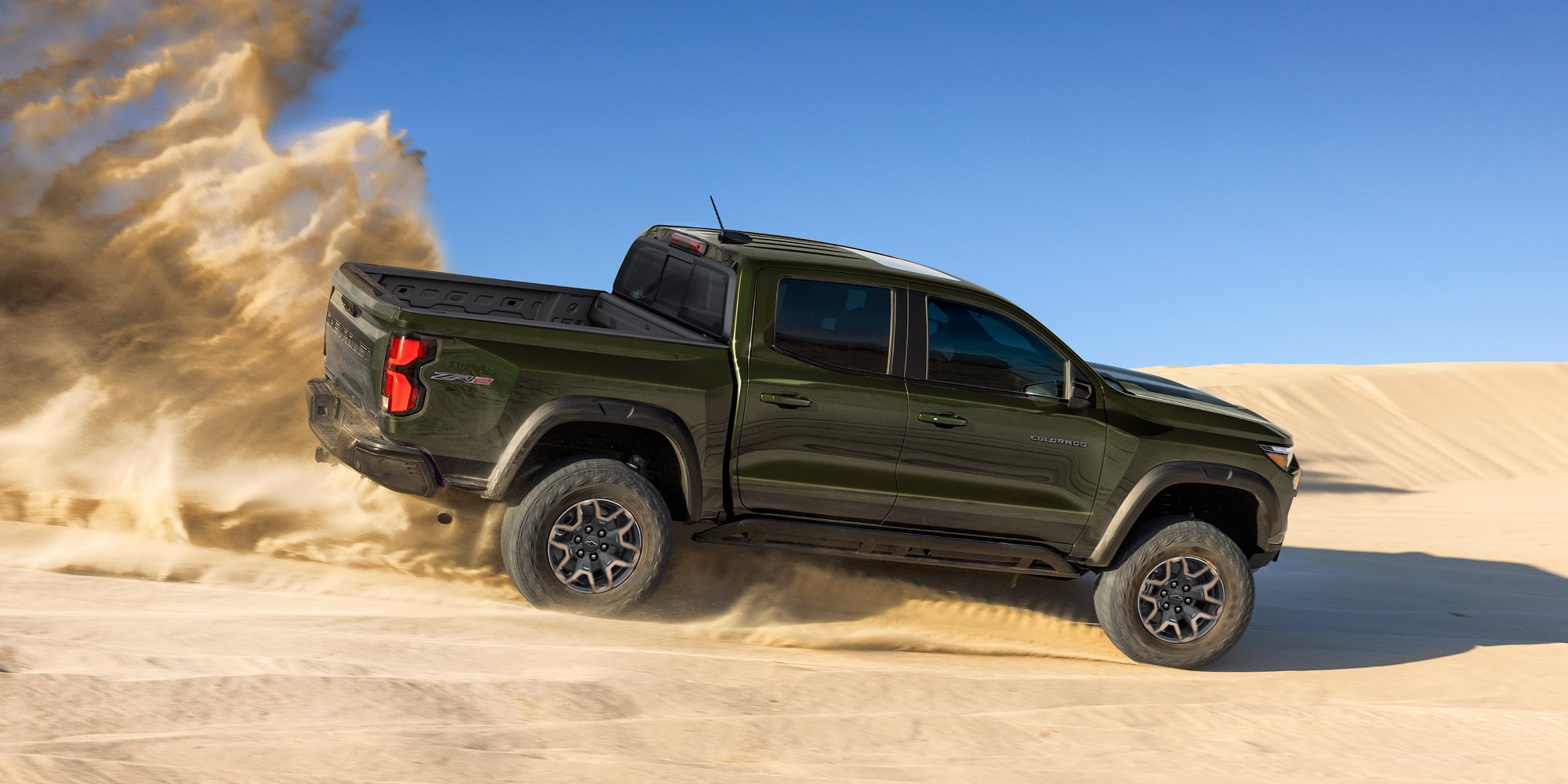 A Black Chevy Colorado Driving Across Sandy Terrain With Dust Trailing Behind the Truck.