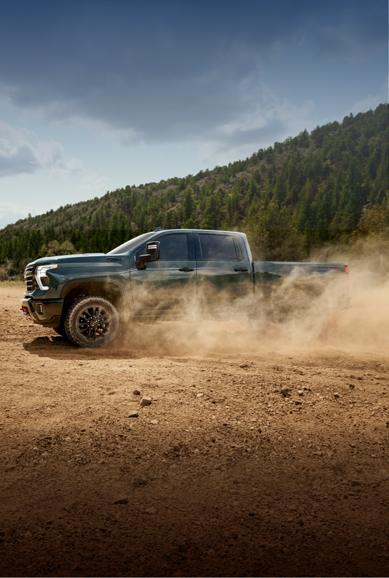 A Green Chevy Silverado HD Driving Across a Dusty Off-Road Trail With Dirt Clouds Surrounding the Vehicle and the Text “CAN’T WAIT?” Displayed Above