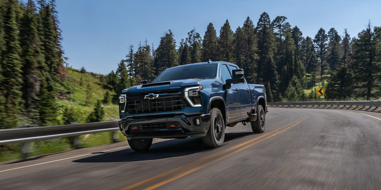 A Black Chevy Silverado HD Driving Along a Curving Mountain Road Surrounded by Evergreen Trees and Forested Hillsides