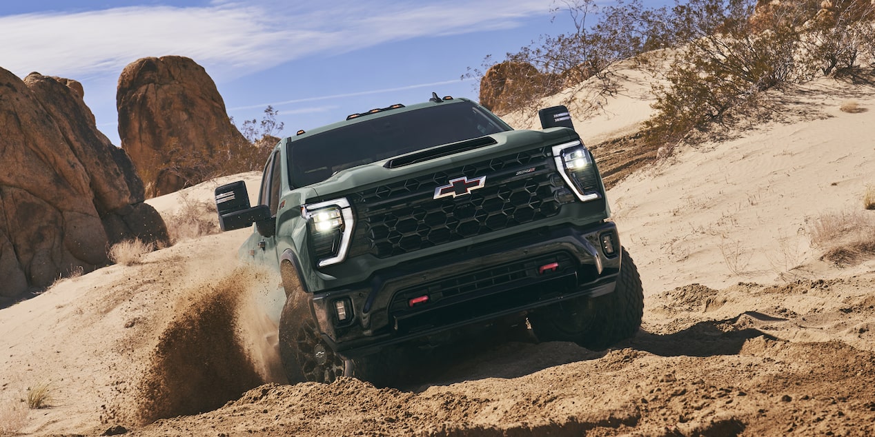 A Chevy Silverado HD Driving Through Deep Sand in a Desert Off-Road Environment With Dust and Sand Kicking Up Around the Truck