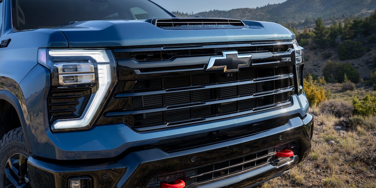 A Close-Up View of the Front Grille and Headlamp Design on a Blue Chevy Silverado HD With Red Tow Hooks Visible Below the Bumper
