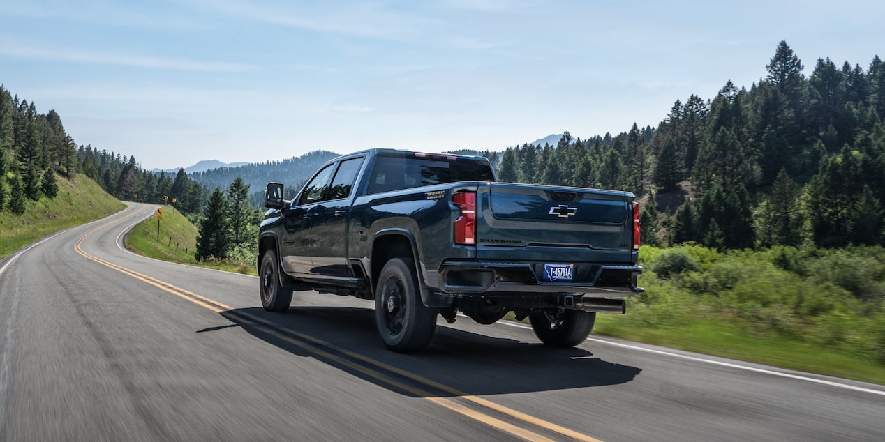 A Black Chevy Silverado HD Driving Along a Scenic Rural Highway Surrounded by Evergreen Trees and Rolling Hills
