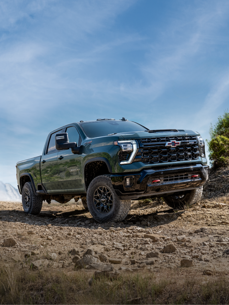 A Black 2027 Chevy Silverado HD Climbing a Rocky Dirt Trail Beneath a Blue Sky With New 2027 Silverado HD Text Displayed Above the Vehicle