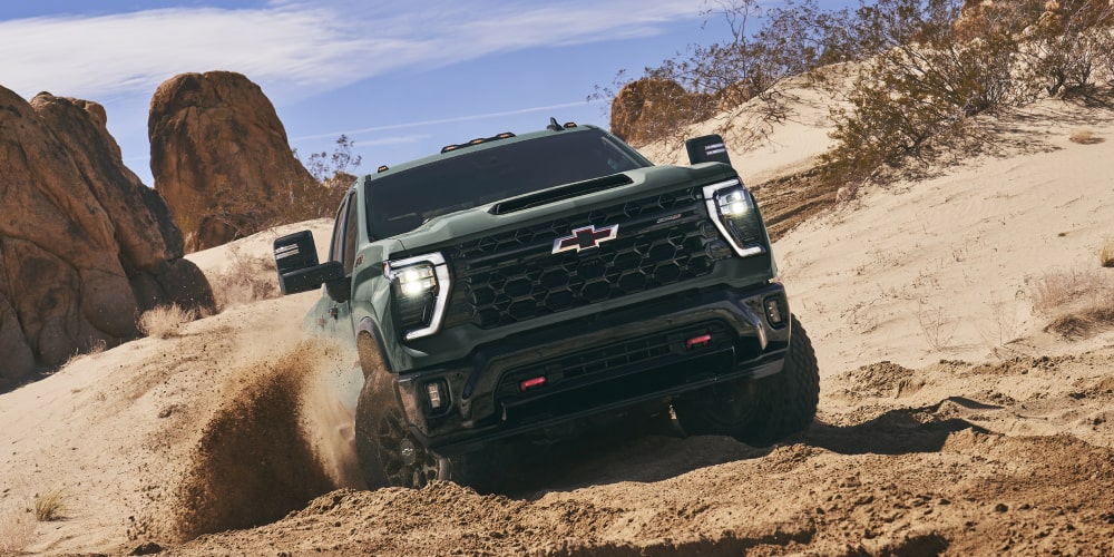 A Chevy Silverado HD Traversing a Deep Sandy Off-Road Trail Between Large Rock Formations in a Desert Environment