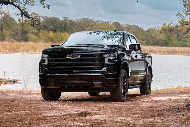 Front Three-Quarter View of a Black Chevrolet Silverado LD High Country Parked Near a Lakeshore With Natural Woodland Scenery in the Background.
