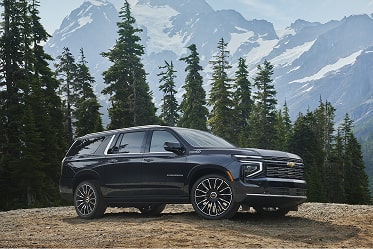 Front Three-Quarter View of a Black Chevrolet Tahoe High Country Parked in Front of a Modern Wood-Clad Home With Mountain Landscape Surroundings.