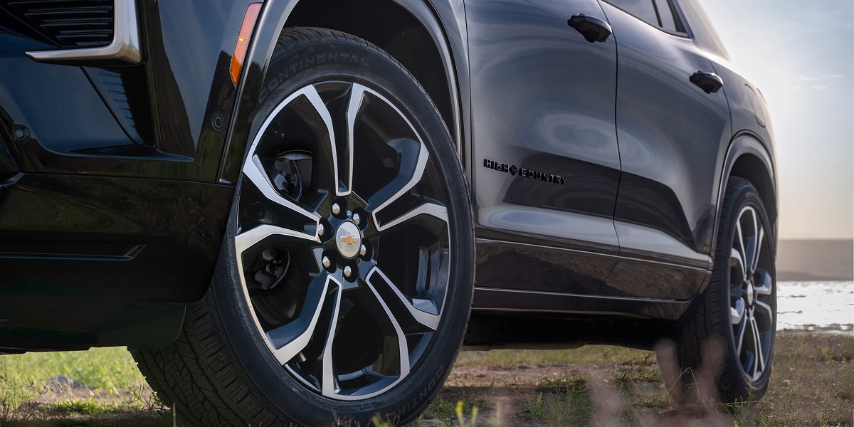 Close-Up of a Chevrolet Traverse High Country Wheel Featuring a Multi-Spoke Alloy Rim Design, All-Season Tire, and Black Exterior Body Panels in an Outdoor Setting.
