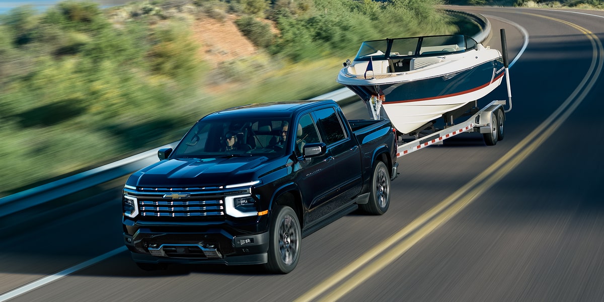 Chevrolet Silverado High Country Towing a Boat Trailer Along a Scenic Two-Lane Road With Rolling Hills in the Background.