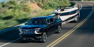 Chevrolet Silverado High Country Towing a Boat Trailer Along a Scenic Two-Lane Road With Rolling Hills in the Background.