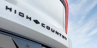 Close-Up of the Chevrolet High Country Tailgate Badge and Signature Red Accent Lighting Against a Blue Sky Background.