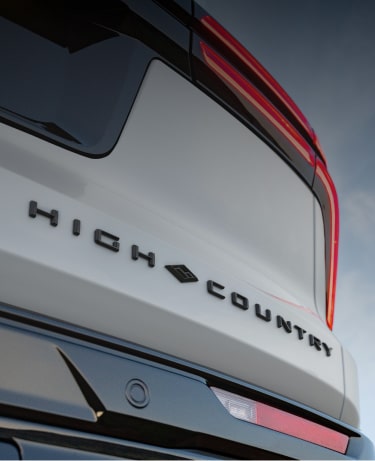 Close-Up of the Chevrolet High Country Tailgate Badge and Signature Red Accent Lighting Against a Blue Sky Background.