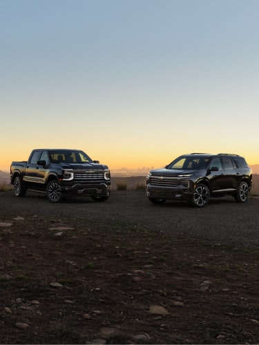 Chevrolet Silverado High Country and Chevrolet Traverse High Country Parked on a Rugged Dirt Landscape at Sunset Beneath a Clear Evening Sky.