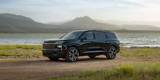 Front Three-Quarter View of a Black Chevrolet Traverse High Country Parked on a Dirt Road With a Lake and Mountain Peaks in the Background.