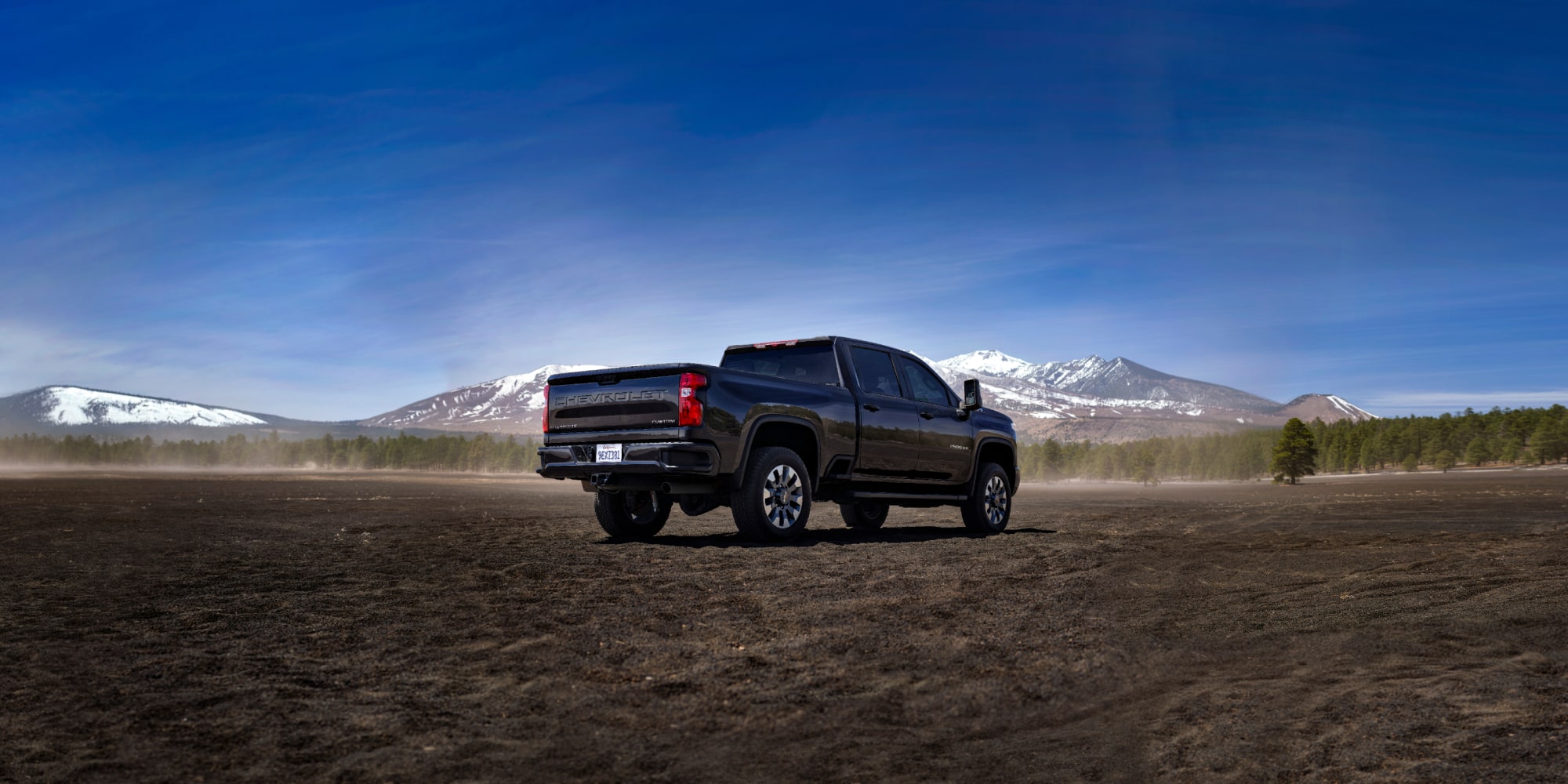 A Black Chevy Silverado LD Driving Across an Open Field with Snow-Capped Mountains in the Distance.