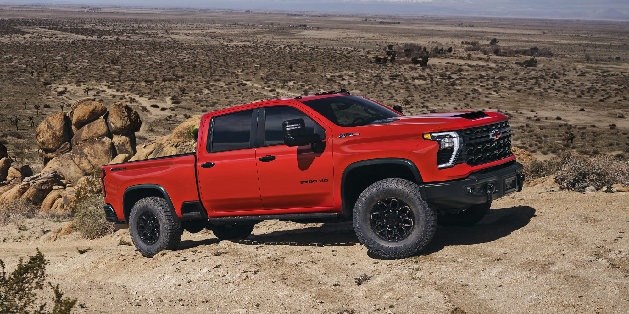 A Red Chevy Silverado LD Parked on Rocky Desert Terrain Under a Clear Blue Sky.