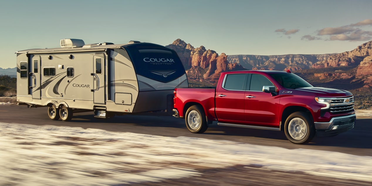 A Red Chevy Silverado 1500 Pickup Truck towing an RV Down a Highway.