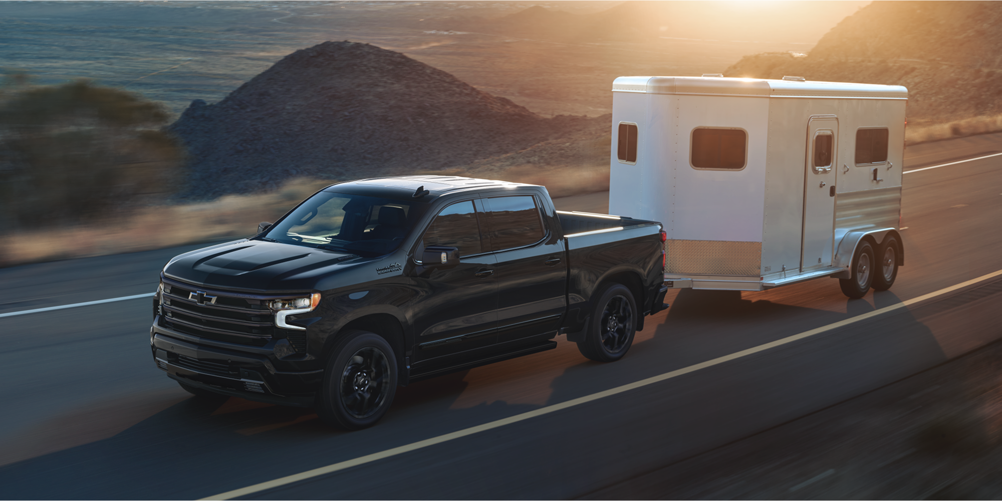 A Chevy Silverado 1500 Pickup Truck Towing a Small Trailer Down a Highway.