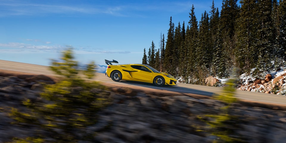 Side View of a Yellow Chevy Corvette ZR1 Driving on a Road with a Downward Slope Surrounded by Trees