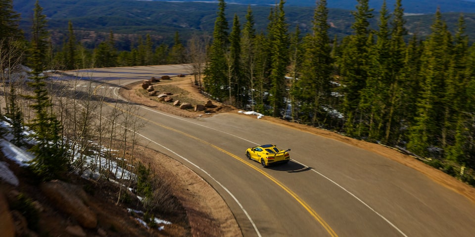 Far Away Overhead Rear View of a Yellow Chevy Corvette ZR1 Driving Down the Road with Trees on Both Sides