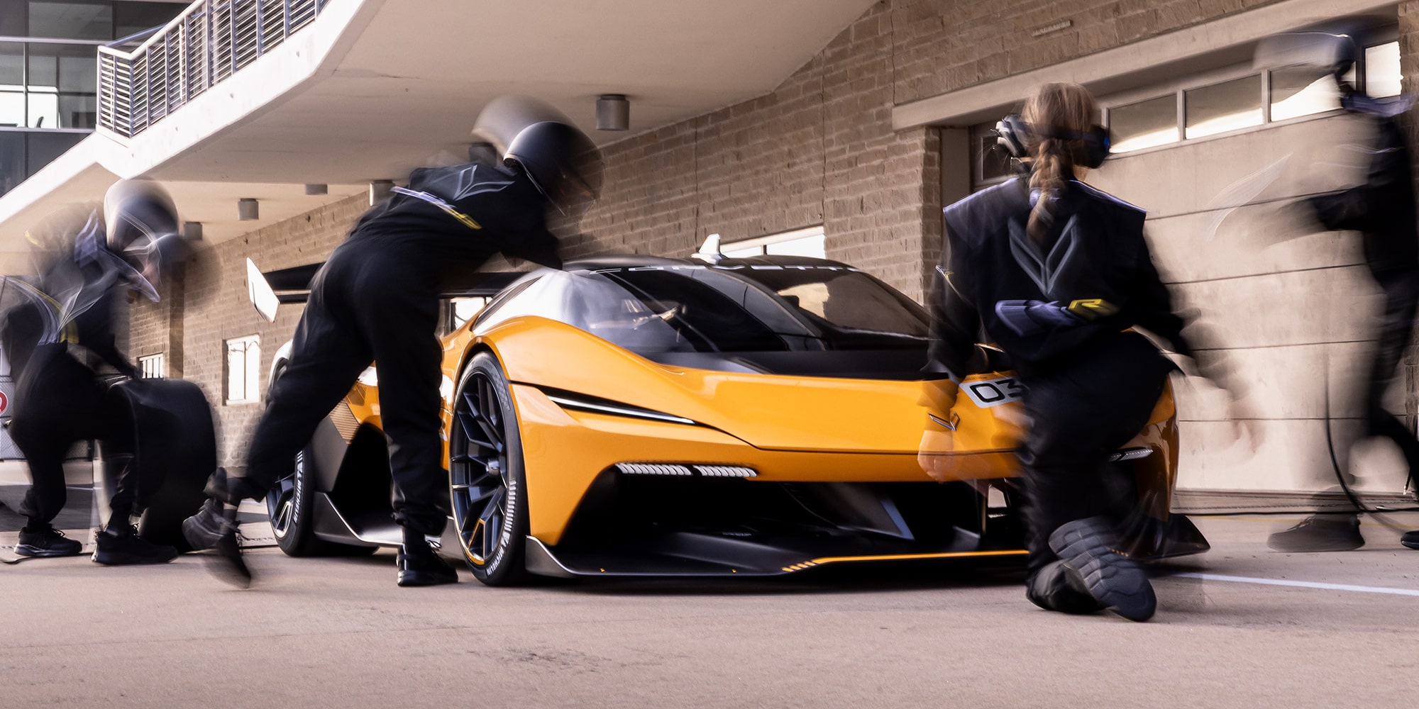 Front passenger side view of a 2026 Corvette CX.R surrounded by a pit crew outside of a garage