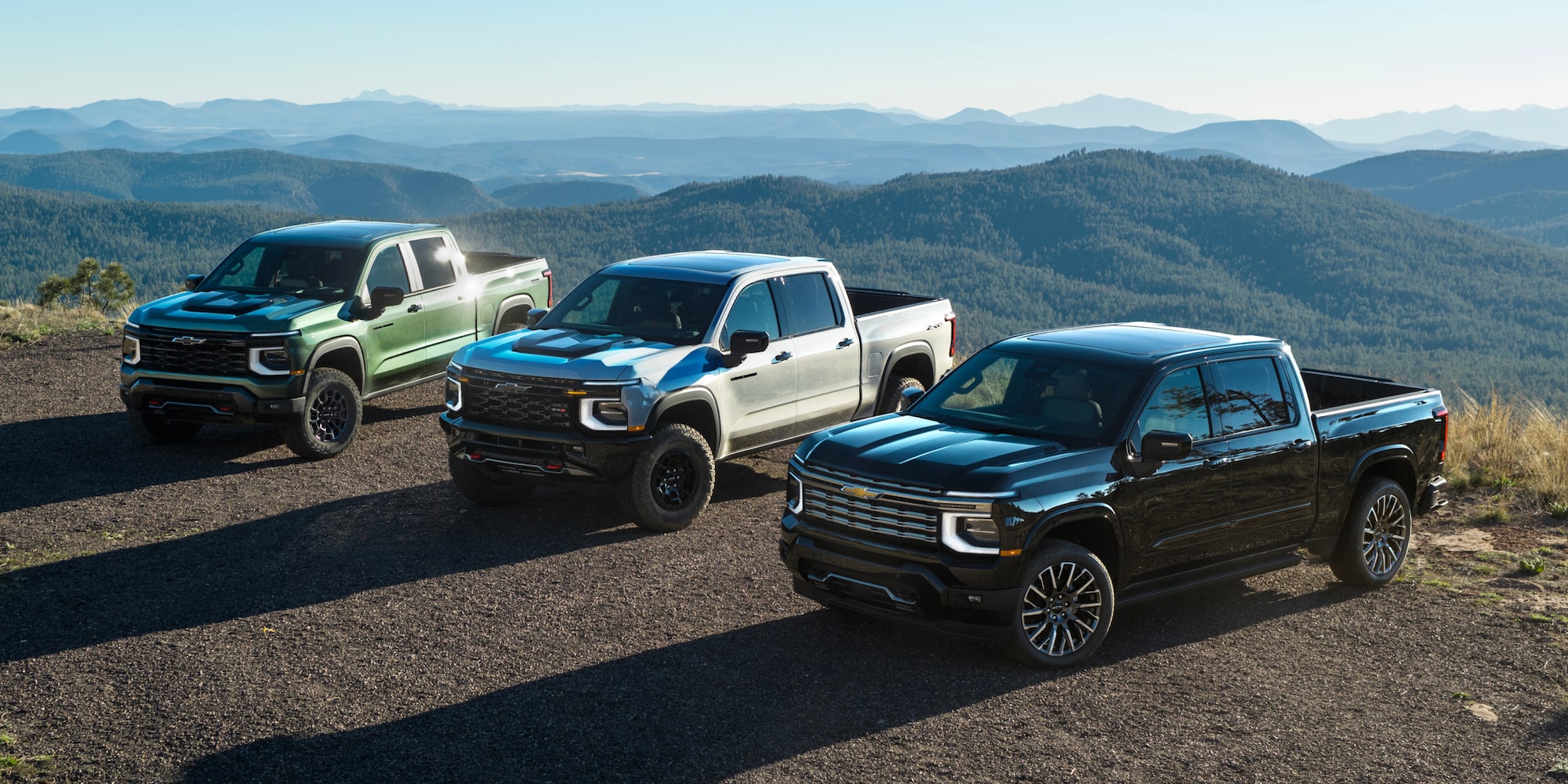 Three Chevy Silverado 1500 Trucks Lined Up at the Top of a Mountain with the Sun Shining Behind Them