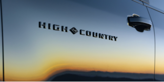 Three Quarters View of a White 2026 Chevy Colorado Driving through a Dust Cloud on a Desert