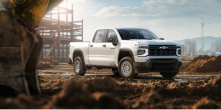 Three Quarters View of a White 2026 Chevy Colorado Driving through a Dust Cloud on a Desert