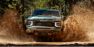 Three Quarters View of a White 2026 Chevy Colorado Driving through a Dust Cloud on a Desert