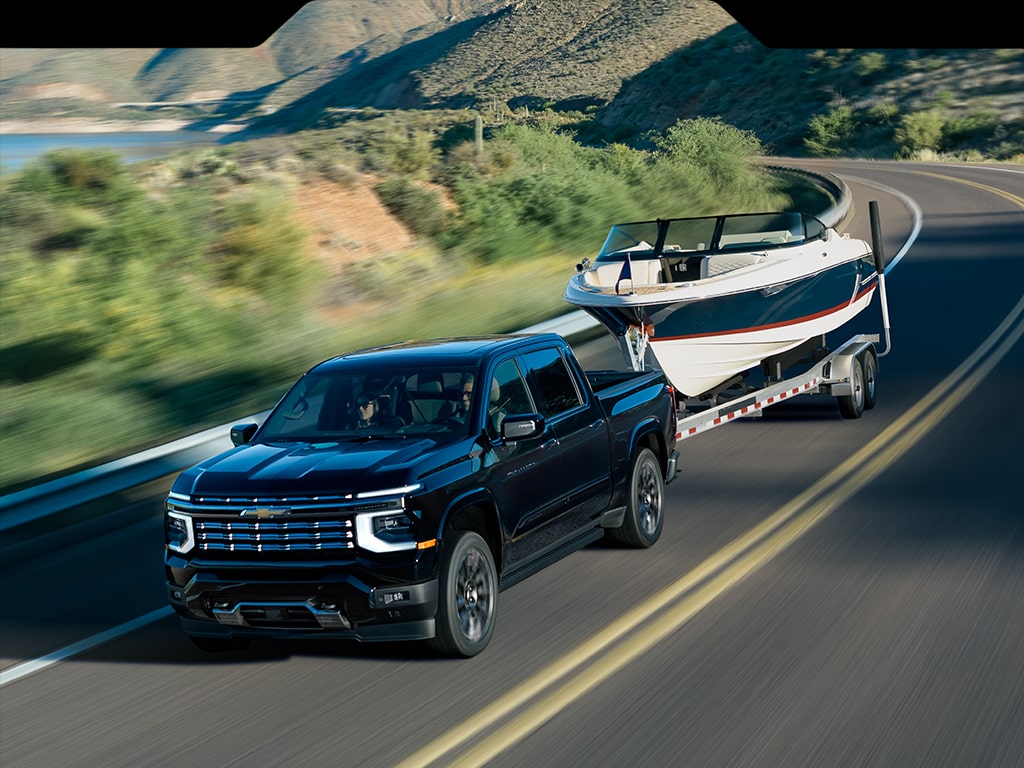 A 2027 Chevy Silverado 1500 High Country towing a boat alongside a lake