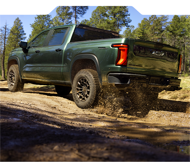 A 2027 Chevy Silverado 1500 Towing a Boat and Driving Around the Curve of a Road Next to a Lake