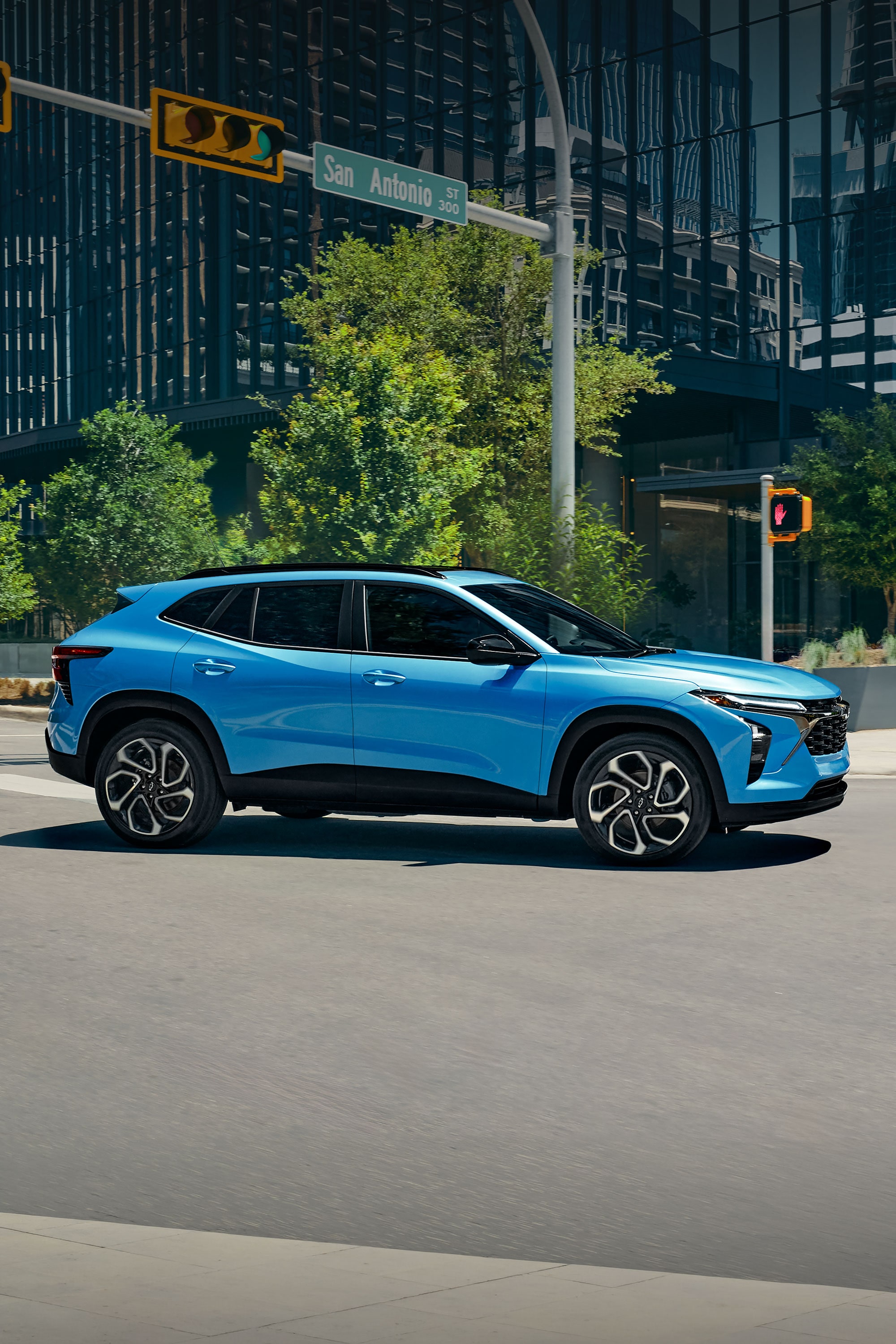 A Blue Chevy Trax Parked in an Urban Setting With Modern Buildings and Trees in the Background.