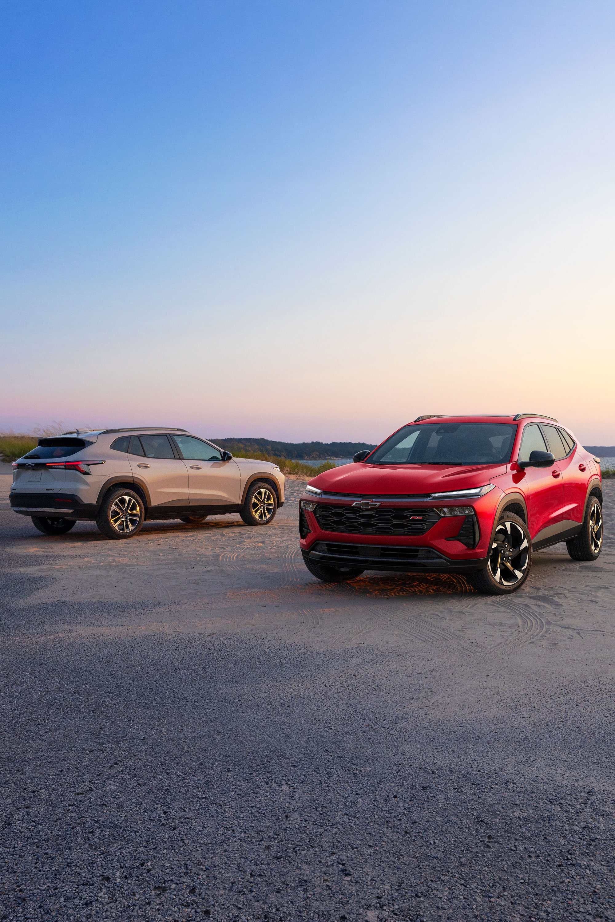 Chevy Trax RS en Rojo y Chevy Trax ACTIV en Plata estacionadas lado a lado en un camino costero al atardecer.