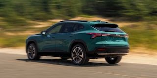 A Blue-Green Chevy Trax Driving Along a Sunlit Road With Trees Blurred in the Background.