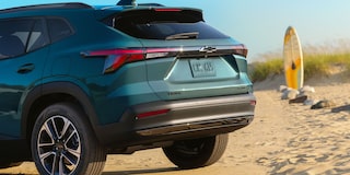 A Rear Three-Quarter View of a Chevy Trax Parked on a Beach With a Surfboard Standing Nearby.