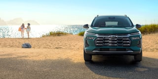 A Front View of a Chevy Trax Parked Near the Coast With Beachgoers Walking Along the Shore in the Background.