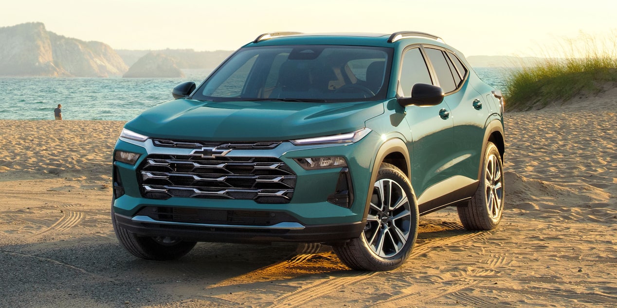 A Chevy Trax Parked on a Sandy Beach With Ocean Water and Coastal Cliffs in the Background.