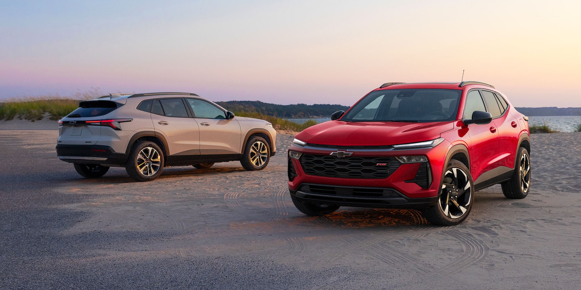 A Red Chevy Trax RS and a Silver Chevy Trax ACTIV Parked Side by Side on a Coastal Road at Sunset.