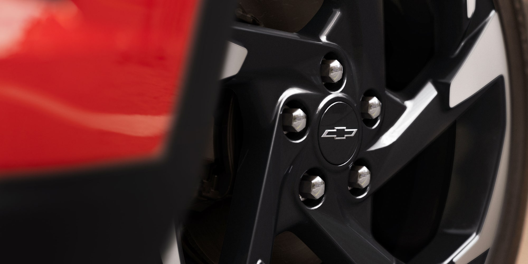 A Close-Up of a Black Alloy Wheel Featuring a Chevy Logo Center Cap on a Red Chevy Trax.