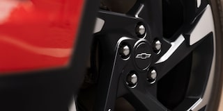 A Close-Up of a Black Alloy Wheel Featuring a Chevy Logo Center Cap on a Red Chevy Trax.