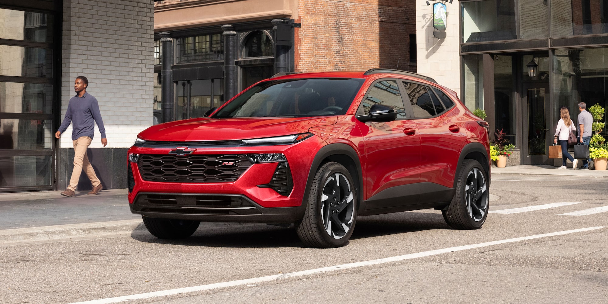 A Red Chevy Trax Parked Along a City Street in Front of Modern Buildings.