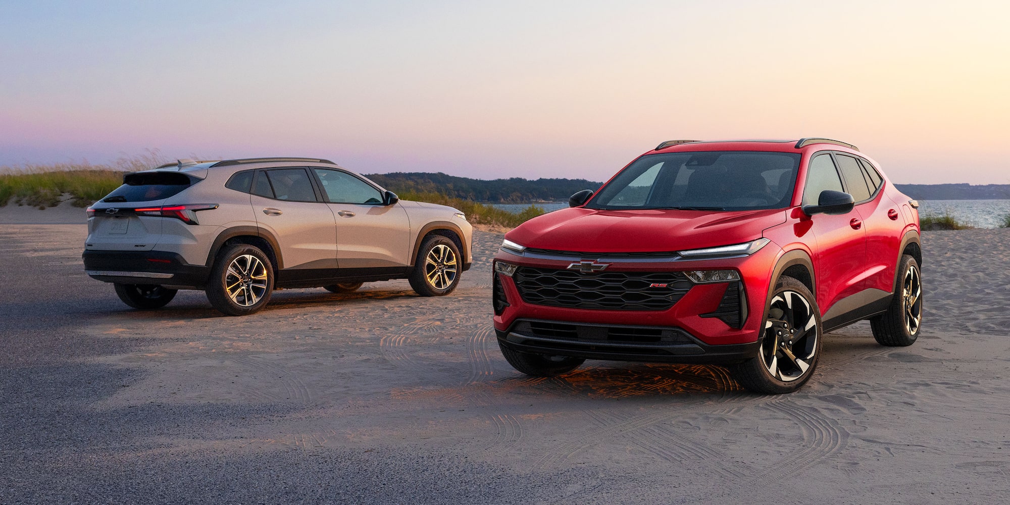 A Red Chevy Trax RS and a Silver Chevy Trax ACTIV Parked Side by Side on a Coastal Road at Sunset.