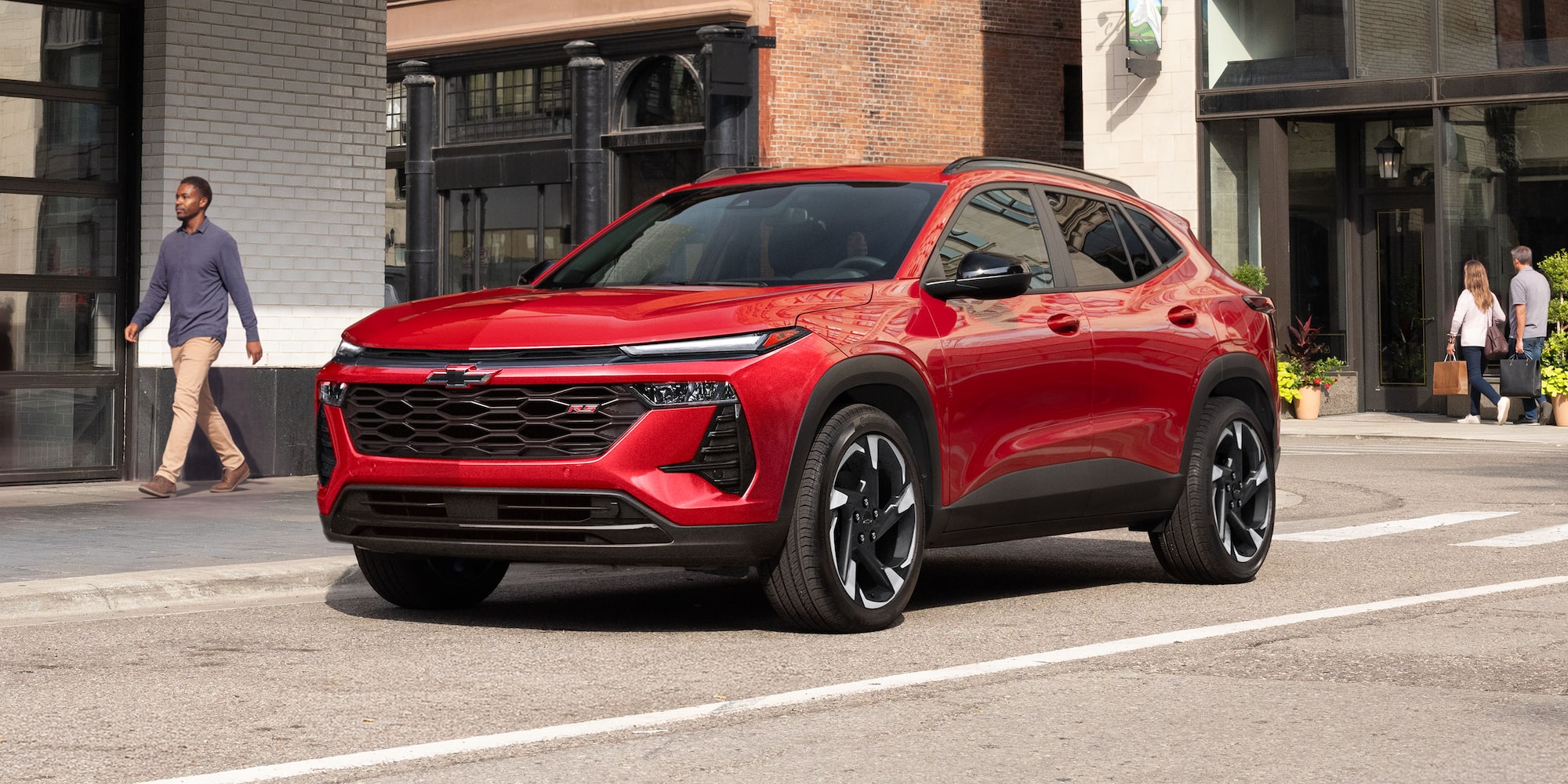 A Red Chevy Trax Parked Along a City Street in Front of Modern Buildings.