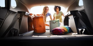A View From the Chevy Trax Cargo Area Looking Toward Two People Standing Behind the Open Liftgate With Travel Bags and Luggage Inside the Vehicle.