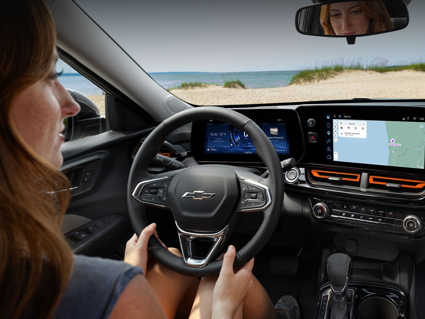 A Driver Using the Chevy Trax Infotainment Touchscreen and Digital Displays While Seated Behind the Steering Wheel.