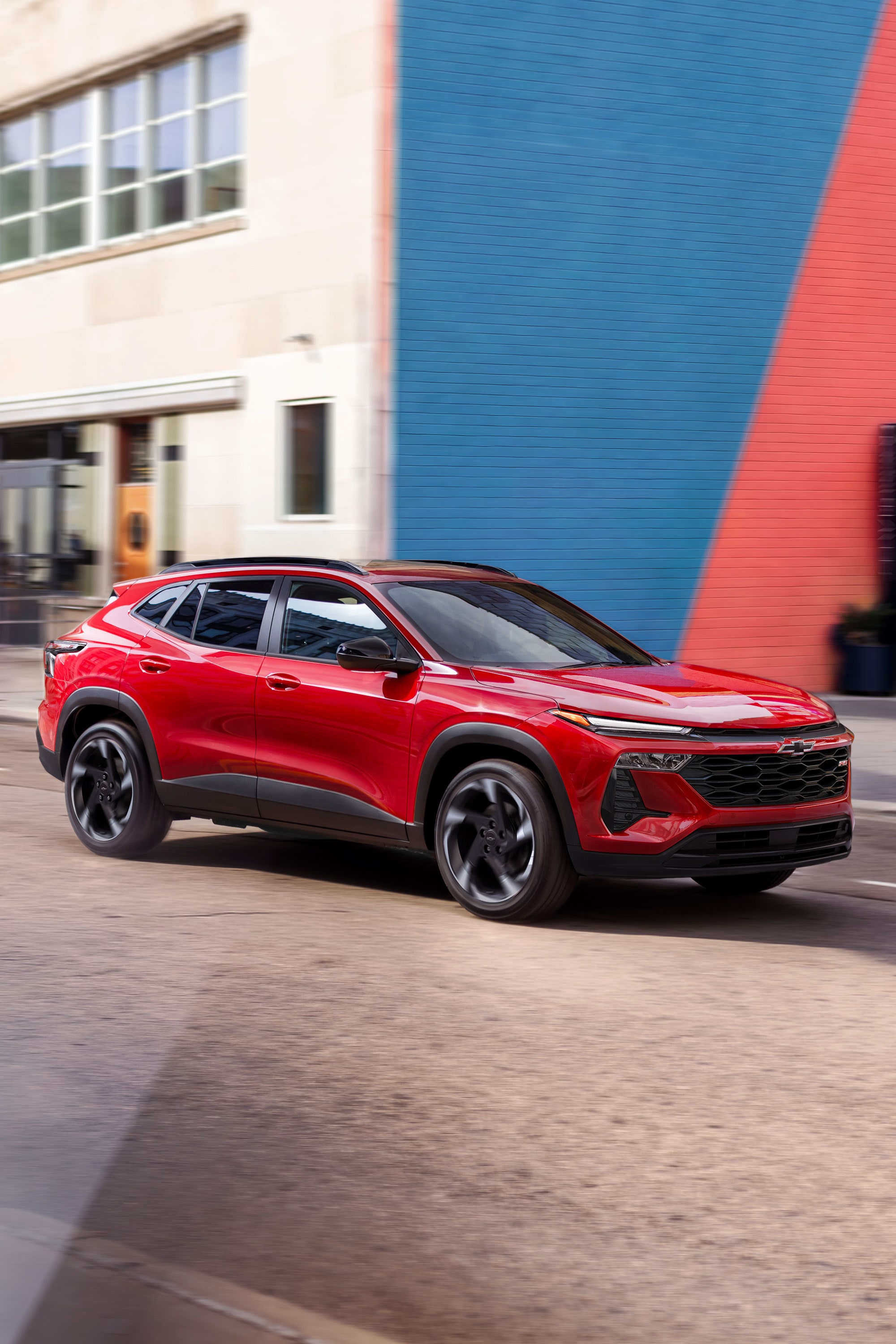 A Red Chevy Trax Driving Through a City Street Surrounded by Contemporary Buildings and Urban Architecture.