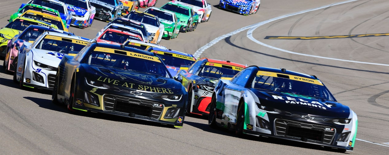 A Pack Of Chevy Race Cars Speeds Down the Track With A Black And Gold Chevy Leading the Tight Formation During A High-Intensity NASCAR Race.