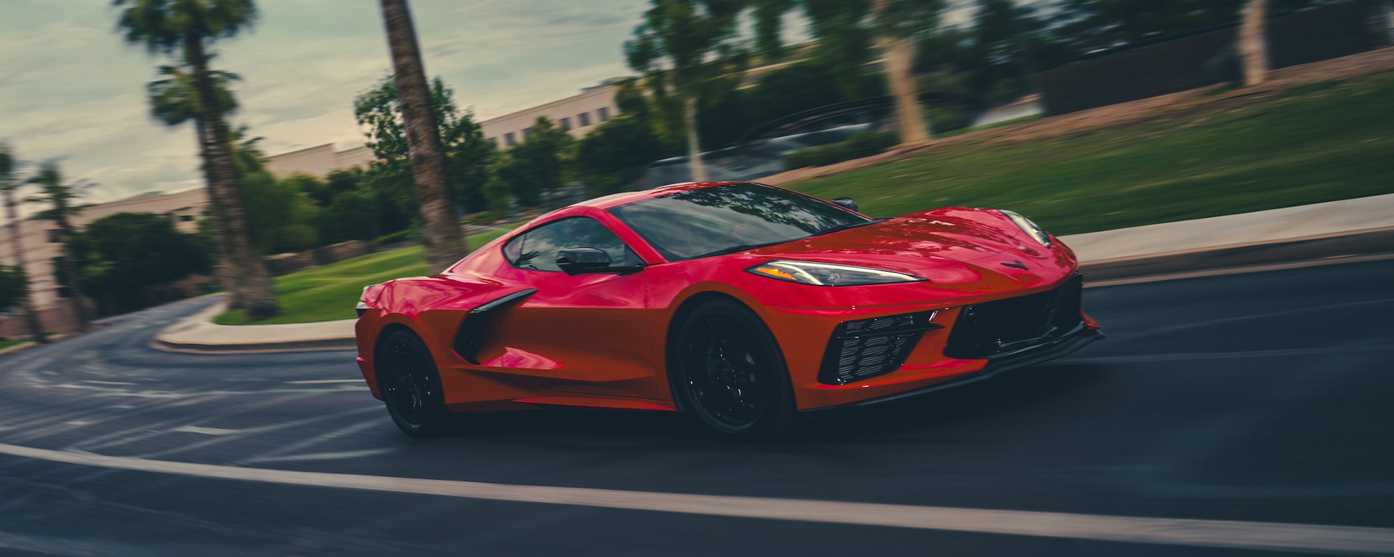 A Red Chevrolet Corvette Driving Down a Road with Palm Trees in the Background