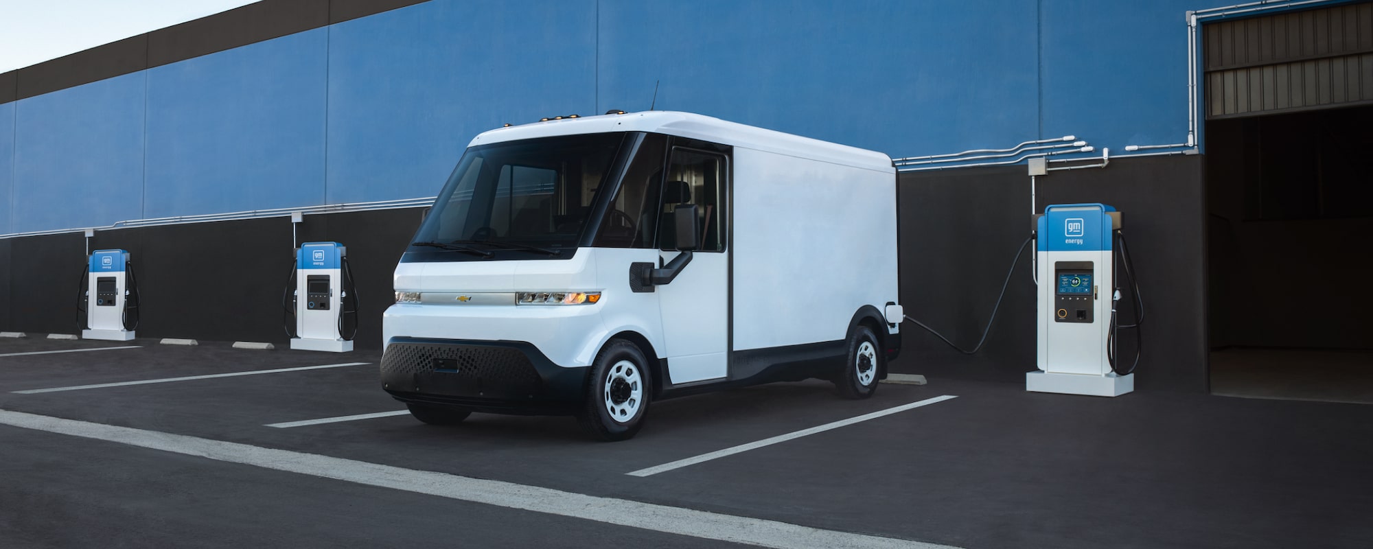 A Chevrolet BrightDrop electric van parked beside charging stations at a depot