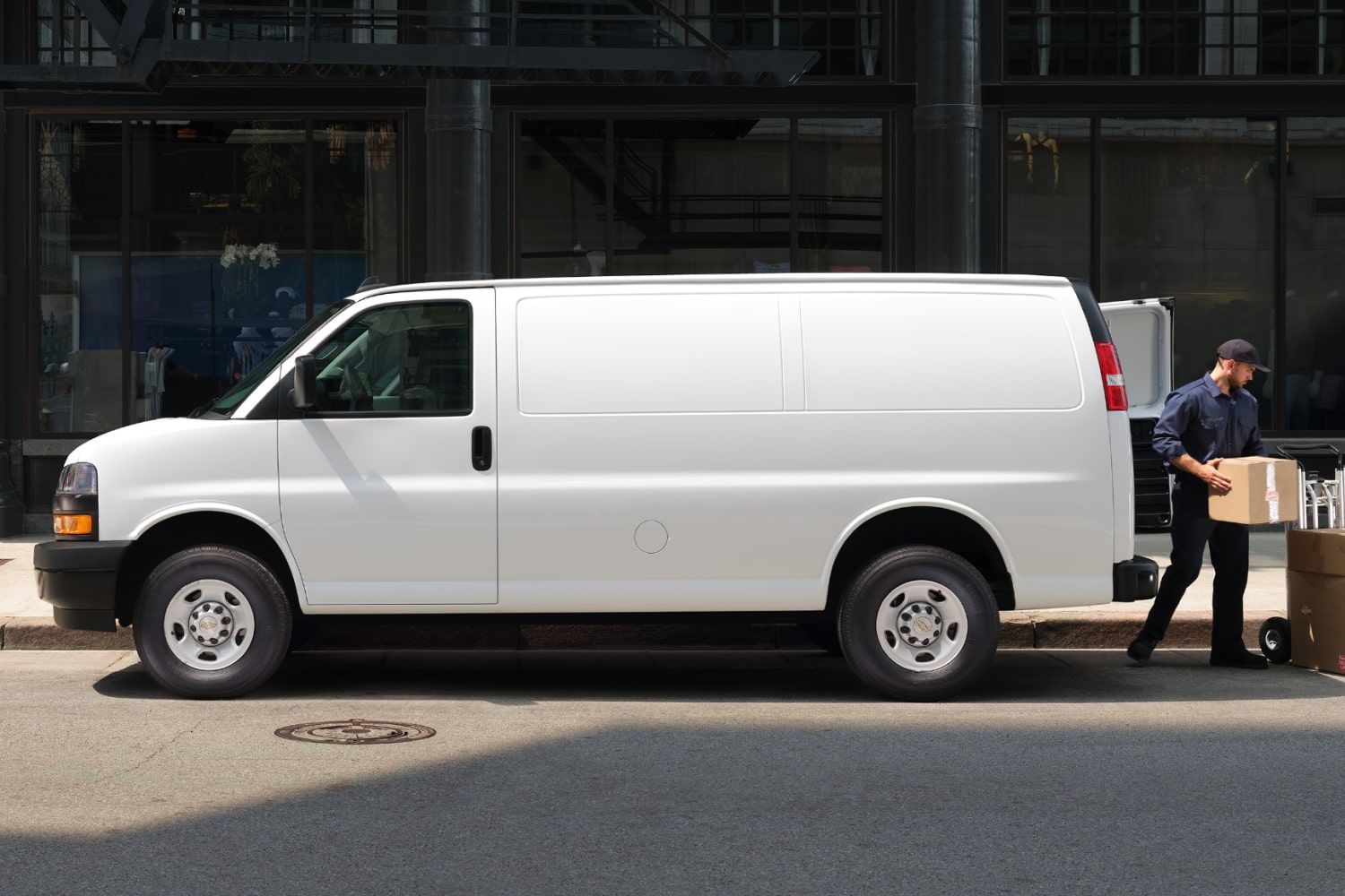 A white Chevrolet Express cargo van at the curb as a worker unloads boxes